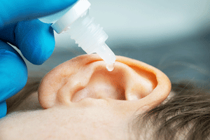 a person laying horizontally with focus on their ear with a tube of Hydrogen Peroxide going into the ear